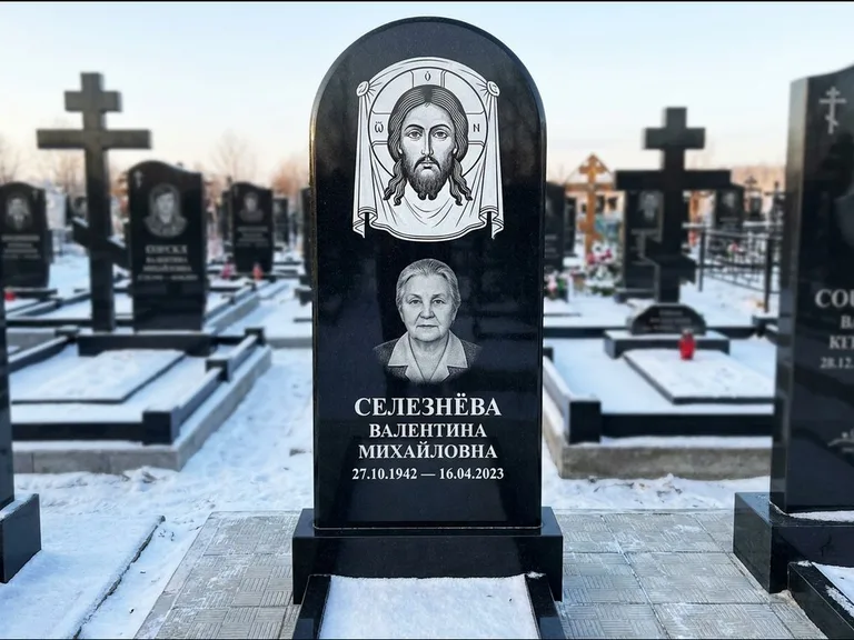 Памятник с гравировкой иконы: небольшая скромная одиночная стела с именной иконой — золочёный нимб на образе, аккуратный участок с газоном, работа «Ковалёв» в Альметьевске
