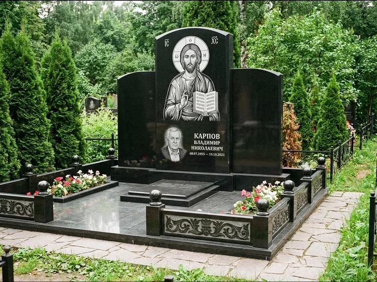 Памятник с гравировкой иконы: широкая панорамная стела с золочёным нимбом — гравировка образа Матроны Московской, цветник с белыми хризантемами, работа «Мельникова» в Альметьевске