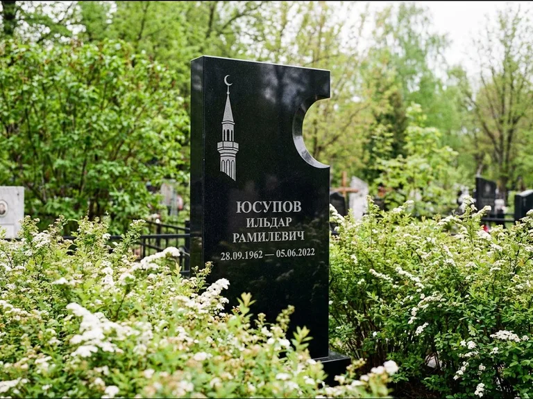 Мусульманский памятник с гравировкой мечети: стела с боковым вырезом в форме полумесяца — гравировка минарета с полумесяцем, низкие кусты спиреи в цвету, работа «Юсупов» в Альметьевске